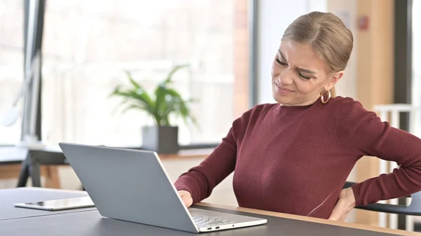 Mladá žena s bolestí zad pomocí notebooku v kanceláři — Stock fotografie
