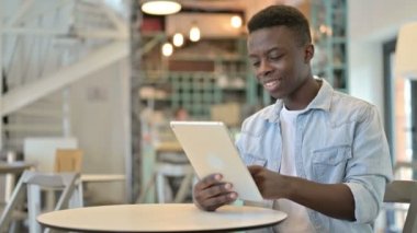 Cafe 'de Tablet üzerinde çalışan neşeli Afrikalı genç adam.
