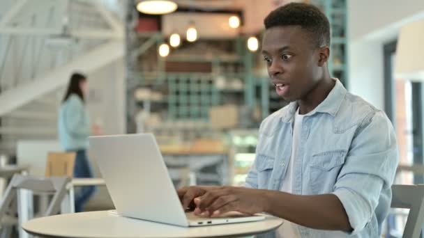 Joven africano positivo celebrando el éxito en el ordenador portátil en Café — Vídeo de stock