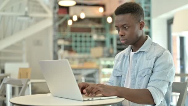 Perturbado joven africano hombre reaccionando a la pérdida en el ordenador portátil en Café — Vídeos de Stock