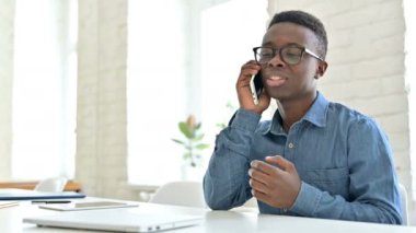 Ofiste akıllı telefondan konuşan gülümseyen Afrikalı genç adam. 
