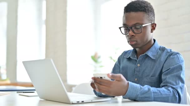 在办公室使用笔记本电脑和智能手机的专注的非洲年轻人 — 图库视频影像