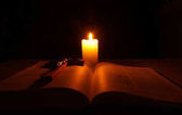 Hořící svíčka, otevřené Bibli a krucifix na stole