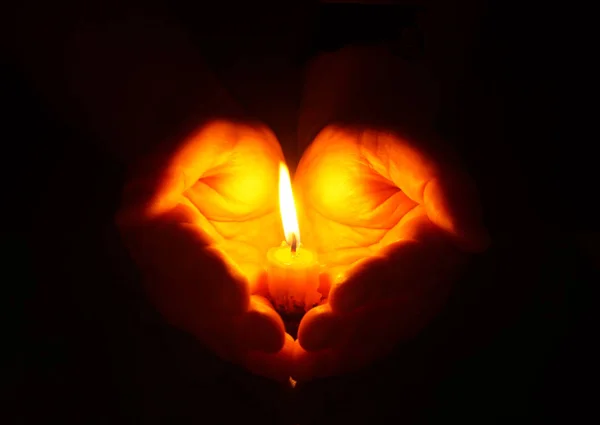 Mãos e vela acesa no escuro — Fotografia de Stock