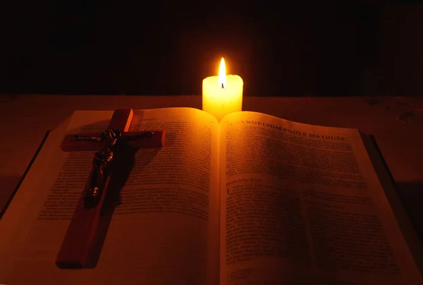 Burning candle, bible and crucifix on desk