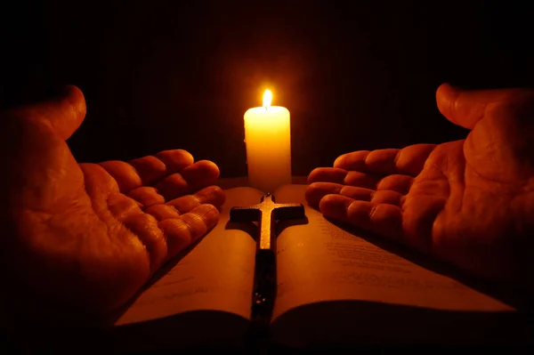 Burning candle, open Bible and prayer hands