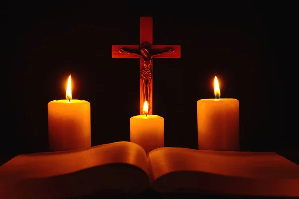 Распятие и три горящих свечи с открытой библией на столе в т — стоковое фото