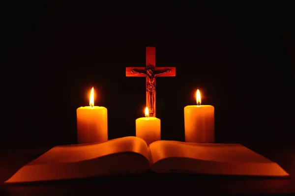 Распятие и три горящих свечи с открытой библией на столе в т — стоковое фото