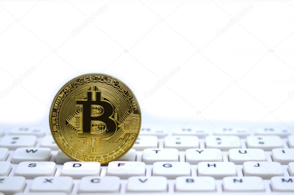 Golden symbolic coin of bitcoin on white keyboard.