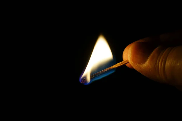 Burning match in a hand on black background.