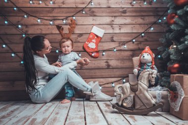 Genç anne ve onun bebek arayıcısı oturma xmas ağacı