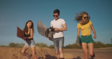 Yaz yaşam tarzı. Snowboard yapan üç genç insan koşuyor ve kameraya kum atıyor. Tasasız gençler birlikte eğleniyorlar. Özgürlük, spor, ekstrem, kum kaykayı, seyahat, turizm, tatil konsepti.