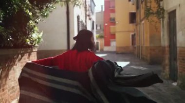 Bahar yaşam tarzı. Güneşli bir günde binalar arasında yürüyen Asyalı güzel bir kadın. Gülümseyen kız kamerada yavaş çekimde flört ediyor. Eski İtalya caddesinde güzel bir kadın. Hafta sonu ve tatil.