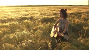 Güneşli yaz sahasında gitar çalan mutlu bir kadın. Beyaz bir bayan şarkı söylüyor ve eğleniyor. Ağır çekim. Küçük gitar. Müzik, doğa, yaşam tarzı konsepti. Müzisyen gitarist bayan gün batımını çalıyor..