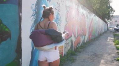 Özgürlük ve yaşam tarzı kavramı. Neşeli kız yürüyor ve havaya sprey boya sıkıyor. Yaratıcı genç grafiti sanatçısı sıcak yaz gününde boyalı duvara karşı eğleniyor. Vahşi ve özgür.