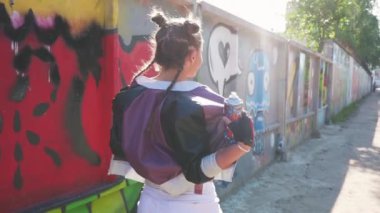 Neşeli kız yürüyor ve havaya sprey boya sıkıyor. Özgürlük ve yaşam tarzı kavramı. Yaratıcı genç grafiti sanatçısı sıcak yaz gününde boyalı duvara karşı eğleniyor. Vahşi ve özgür.