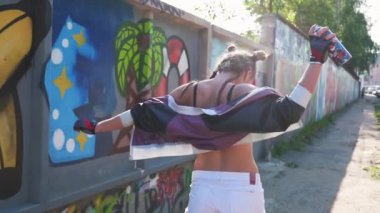 Vahşi ve özgür. Özgürlük ve yaşam tarzı kavramı. Neşeli kız yürüyor ve havaya sprey boya sıkıyor. Yaratıcı genç grafiti sanatçısı boyalı duvarlara karşı sıcak yaz gününde eğleniyor..