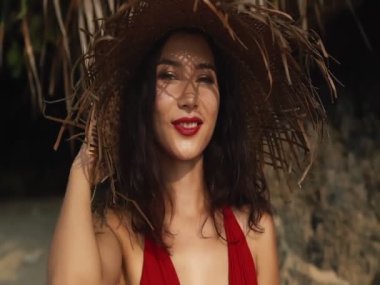 Hasır şapkalı, yaz tatilinde kırmızı elbiseli ve kameraya poz veren ve gülümseyen şehvetli genç bir ırk kadını. Güzellik, seyahat, tatiller, moda konsepti ve yaşam tarzı.