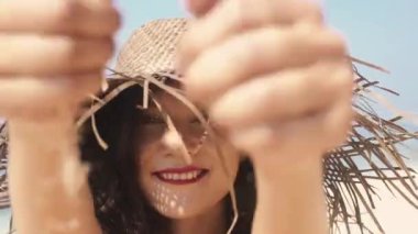 Kırmızı elbiseli güzel bayan cennet adasının tadını çıkarıyor, güneş parlıyor. Romantik ve sakin bir ruh hali. Bali 'nin seyahat yaşam tarzı. Hasır şapkalı neşeli Asyalı kadın parmaklarının arasındaki kumu temizliyor..