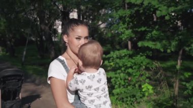 Güzel anne ve küçük oğlu güzel göletin yanındaki parkta yürüyorlar. Gülümseyen anne tatlı çocuğunu kucağında tutuyor. Tatlı çocuk annesinin kolyesiyle oynuyor. Annelik kavramı.