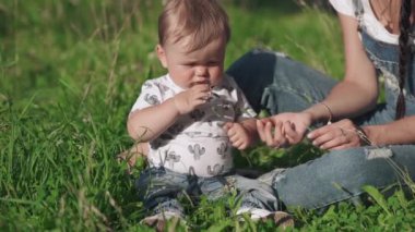 Güzel, genç bir anne tatlı çocuğuna küçük bir çiçek veriyor. Güzel bir anne ve küçük oğlu resim parkında çimlerin üzerinde oturuyorlar. Annelik kavramı, aşk mutluluk ve güzellik..