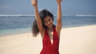 Parmakların arasındaki kumu elleyen neşeli Asyalı kadın. Kırmızı elbiseli güzel bayan cennet adasının tadını çıkarıyor, güneş parlıyor. Bali 'nin tropik atmosferi. Romantik ve sakin bir ruh hali. Seyahat yaşam tarzı.