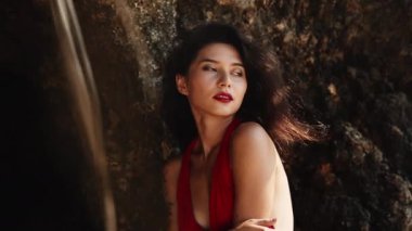 Kırmızı elbiseli, melez bir kadın. Lüks, şehvetli Asyalı kız portresi kameraya gülümsüyor. Sıcak yaz günü, tropik cennet adasında kalırken seksi pozlar. Ticari, müstehcen yaşam tarzı