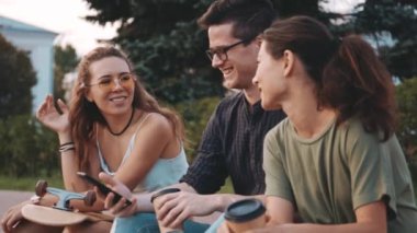 Mutlu gülümseyen öğrenci arkadaşlar üniversite binasının önünde gülüyorlar ve cep telefonlarına bakıyorlar. Üç tane çok ırklı genç insan birlikte vakit geçiriyor. Arkadaşlık, iletişim, gençlik ve yaşam tarzı kavramı