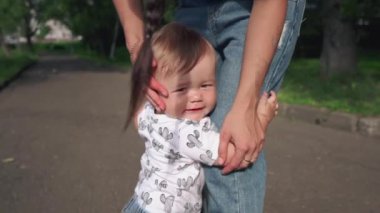 Güzel anne ve küçük oğlu güneşli yaz gününde parkta yürüyorlar. Tatlı çocuk annesinin bacaklarına tutunuyor. Gülümseyen Asyalı anne sevimli çocuğunu kucaklıyor ve seviyor. Aile ve annelik kavramı.