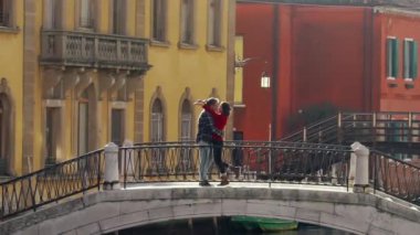 Yakışıklı bir adam, balayı sırasında Venedik köprüsünde duran Asyalı sevgilisini öpüyor ve sarılıyor. Tatili geçirmenin en iyi yolu Avrupa 'ya seyahat etmek..