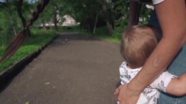 Tatlı çocuk annesinin bacaklarına tutunuyor. Gülümseyen Asyalı anne sevimli çocuğunu kucaklıyor ve seviyor. Güzel anne ve küçük oğlu güneşli yaz gününde parkta yürüyorlar. Aile ve annelik kavramı.