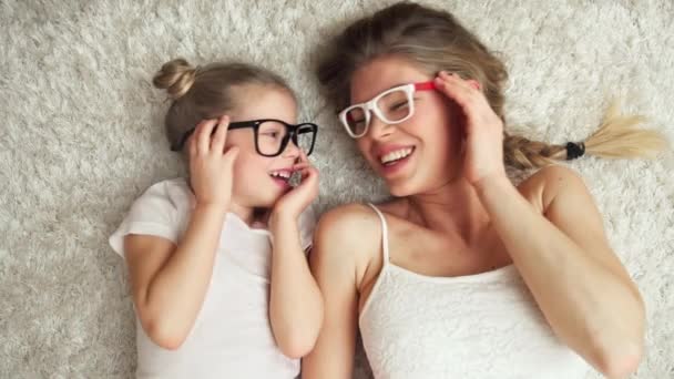 美丽的女孩与她的母亲躺在地毯上 改变眼镜彼此 家庭乐趣在家 — 图库视频影像