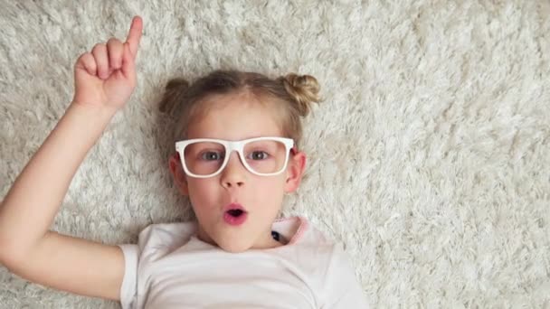 漂亮的微笑的女孩戴着眼镜思考新的想法和笑 可爱的孩子在地板上在家 — 图库视频影像
