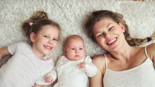 幸せな家族は家の床にリラックス 生まれたばかりの赤ちゃんにキスの娘と若い陽気なママ — ストック動画