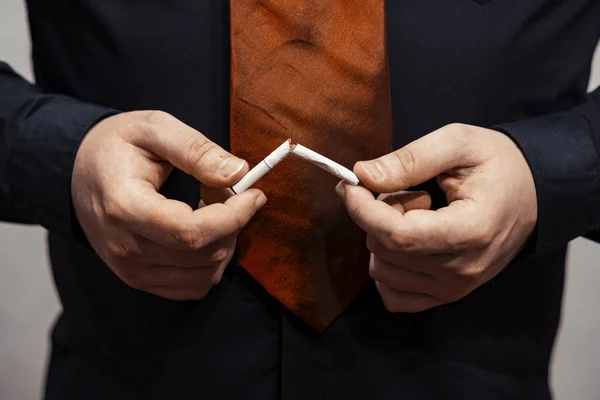 En brækket cigaret er i hænderne på en mand. Rygning forbudt . - Stock-foto