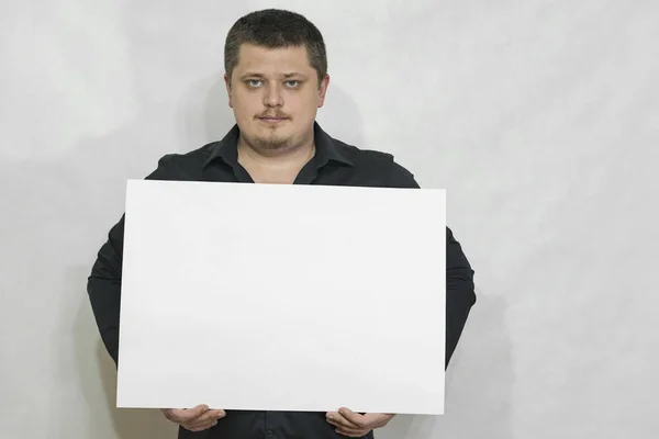 Um homem está segurando um placar vazio ou um quadrado branco de papel. Cara séria. espaço de cópia Imagem De Stock