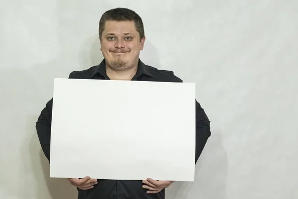 Um homem está segurando um placar vazio ou um quadrado branco de papel. Um sorriso na cara dele. espaço de cópia Fotografia De Stock