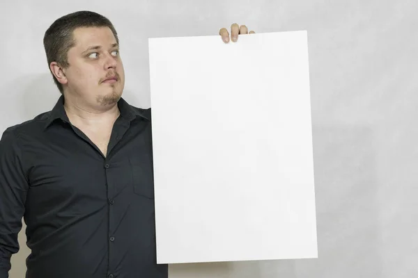 Een man houdt een lege scorebord of wit vierkant papier. Op een witte achtergrond. copyspace Stockfoto