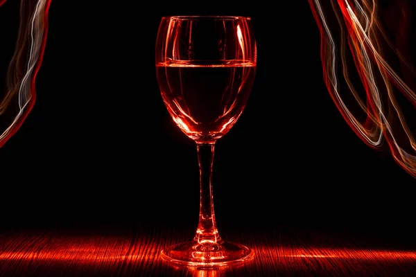Ett genomskinligt glas vin med en vätska. Röd suddig band. Ljuseffekt. — Stockfoto