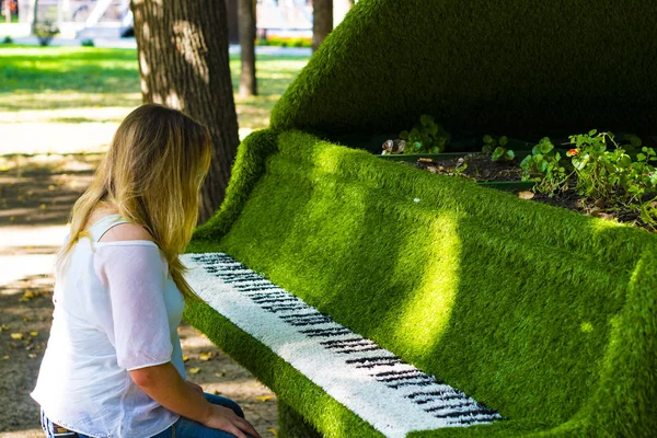 Dívka sedí u klavíru. Žena v brýlích se nachází poblíž záhon v podobě piano. — Stock fotografie