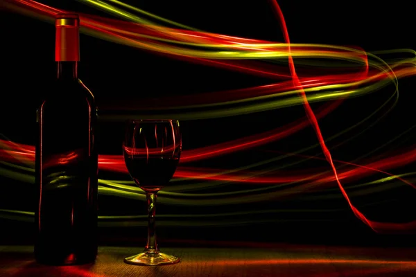 Μπουκάλι και ένα ποτήρι κρασί στο παρασκήνιο με τη μορφή των εφέ φωτισμού. — Φωτογραφία Αρχείου