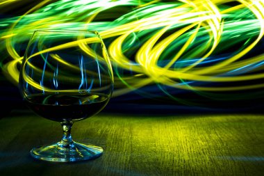 Bir bardak konyak parlak arka plan ışığı efekti üzerinde.