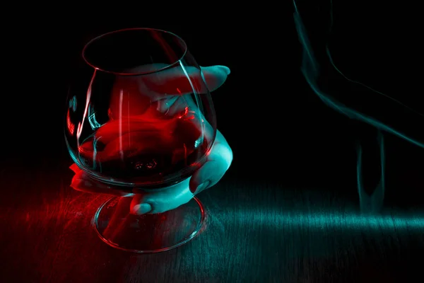 Egy pohár konyak a kezében a sötét háttér. — Stock Fotó