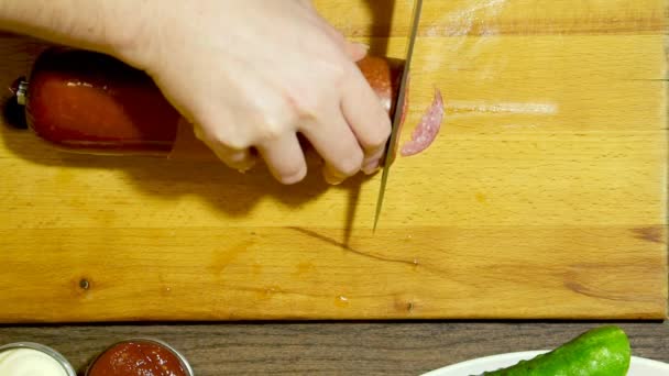 Zbliżenie ludzkich rąk gotowanie jedzenie w kuchni. Cięcie kiełbasy. — Wideo stockowe