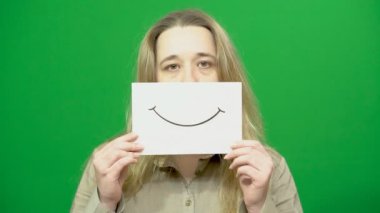 Genç kız poz. Bir kağıt parçası üzerinde mutlu bir surat. Çizilmiş bir atar. Yeşil arka plan. İkiyüzlülük.