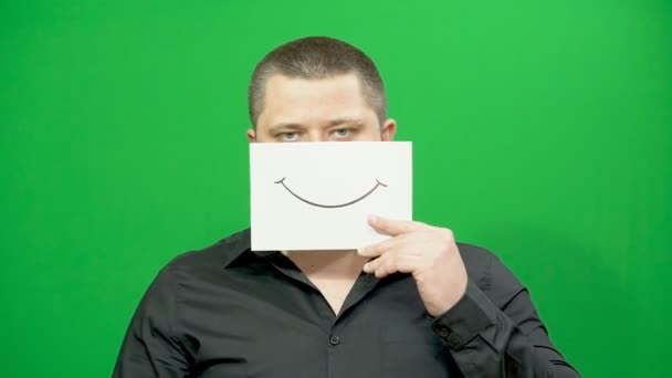 Un joven posando. Sonriente en un pedazo de papel. Cambiando emociones. Hipocresía . — Vídeos de Stock