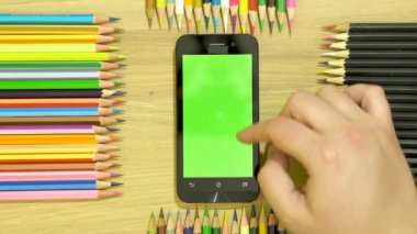 Çevre boyunca masanın üzerine renkli kalemler. Belgili tanımlık smartphone üzerinde el.