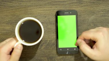 Bir akıllı telefon üzerinde çalışmaya yardım closeup. Ahşap arka plan kahverengi. Öte yandan bir fincan kahve alır.