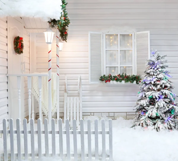 Exterior de invierno de una casa de campo con decoraciones navideñas al estilo americano. Patio cubierto de nieve con un porche, árboles y trineos vintage de madera . — Foto de Stock