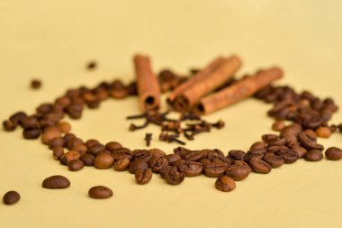 Tarçın kahve çekirdekleri ve karanfil baharat sarı bir arka plan üzerine bir daire içinde üç stickler